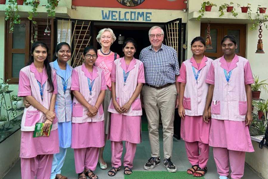 Ein Mann und eine Frau stehen mitb einer Gruppe Frauen in Pflegerkleidung vor einem Krankenhaus